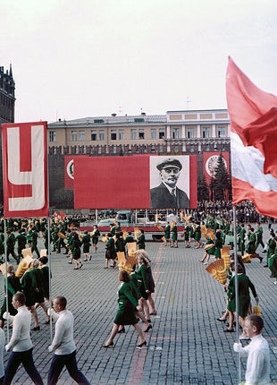 Vintage photograph of a Soviet parade in Red Square, Moscow, showing participants marching past large commemorative banners, Kremlin towers, and ceremonial displays during a major public celebration in the Cold War era.